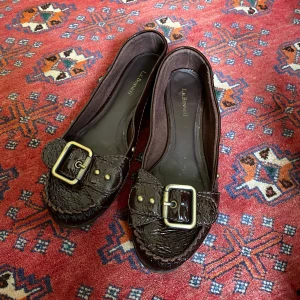 bruna ballerinaskor - mörkbruna ballerinaskor i läder med spänne. strl 40 men skulle uppskatta att dom är 39,5. tyvärr för stora för mig. mycket bra skick.