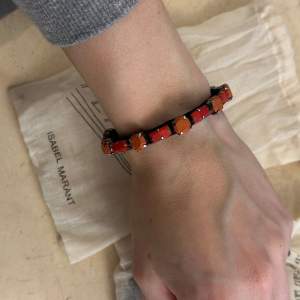 Oanvänt armband med orangea stenar från Isabel Marant. Tillhörande smyckespåse ingår. Armbandets storlek justeras själv. 