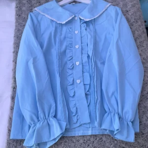 Lolita skjorta  - Jättefin ljusblå lolita skjorta med vit lace krage, volanger och hjärt knappar!  Använd en gång hemma, men aldrig ute. Har inga fläckar/ skador. Storleken är XL men eftersom det är CN är den ungefär som en S-M