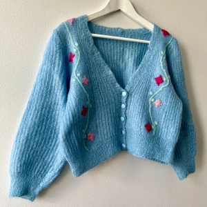 Söt blå kofta med blommor 🌸  - Ljusblå fussy kofta som är något croppad med broderade blommor 🌸 den har ingen storlekslapp men uppskattar att den är M, cropped oversized. Kan passa L beroende på hur en vill att den sitter. Mått i nederkant: ungefär 45cm. Längd: ungefär 43cm. 