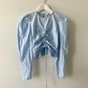 Only. Blå blus med puffärm 🩵 - Ljusblå blus i 100% bomull från only, storlek s. Fin pärlemorsknapp i ryggen, stängs med en dold dragkedja i sidan. Kan justeras framtill med de två snörena. Något sliten i tyget kring dragkedjan, syns på tredje bilden. 
