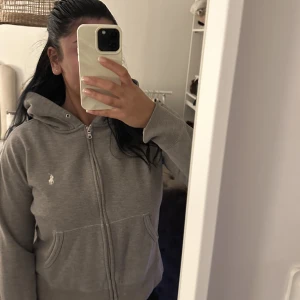 Ralph Lauren zip-hoodie - Jätte fin grå zip hoodie från Ralph lauren. De snygga och unika me denna hoodien är att den har slits på sidorna som gör att den sitter jätte snyggt på!