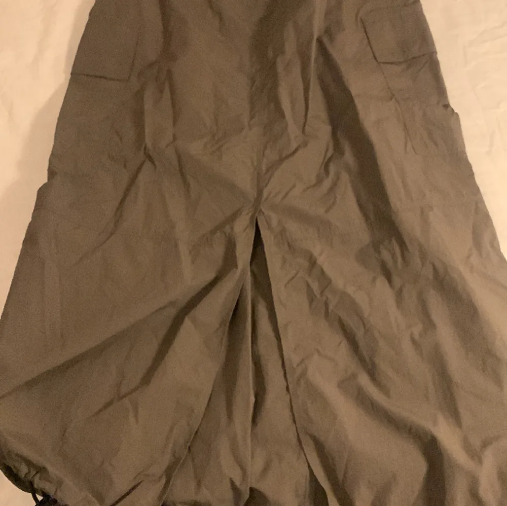 En lång kjol som är i ett tyg som liknar parachute byxor. En grön grå färg. Helt ny. Inga hål och oanvänd. Kjolar.
