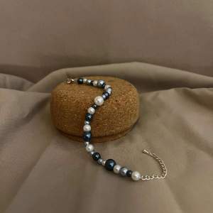 Armbandet Eleonore består av flera olika storlekar av pärlor i olika färger av blått med silver lås och kedja.  Namn: Elonore Längd: Hela 23 cm Pärlor 15,5 cm