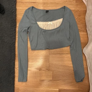 Söt coquette tröja med liten rosett! - Söt tröja som har en grå/blåaktig färg, väldigt fin o rosetten är verkligen cherry on top! Skön material, magtröja dvs inte lång men inte för kort heller. Köp den!!