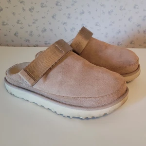 UGG Goldenstar Clog Storlek 38 - Snygga och bekväma UGG-tofflor i beige, färgen heter Driftwood.  Storlek 38.  Fint skick, sparsamt använda. Svarar gärna på frågor eller skickar fler bilder