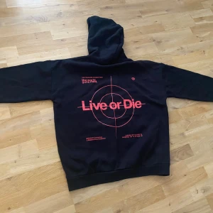 Hoodie stl L  - Aldrig använd endast provad så Fint skick Hoodie strl L  Svart med rött tryck l och röd text se bild 