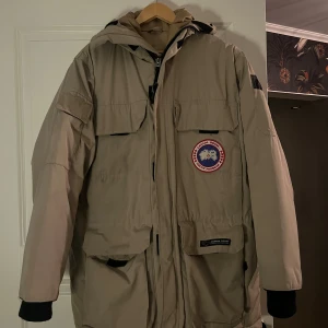 Canada Goose Puffer Jacket - Säljer denna Canada Goose jacka som ej kommer till användning. Den är i bra skick använd med omsorg och inga defekter. Det är beige och rätt oversized, storlek XS, jag skulle mer säga S/M. Nypris ca 12 000