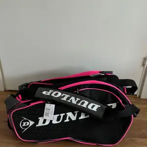 DUNLOP ELITE PINK THERMOBAG padel väska sälje. Ny, oanvänd, men lapp kvar. Svart/rosa.  Gott om plats och samtidigt stilig väska. Tre stora fack för rack och ett separat skofack (dvs separat från kläderna). Termoisolerad. Robust. Bekväma vadderade ha