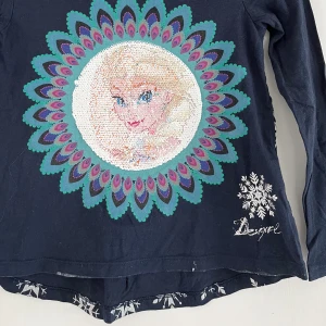 Frost tröja från Desigual - Cool frosttröja med paljetter som visar Anna eller Elsa beroende på hur de ligger. Baksidan har snöflingor i silver. Fint skick!