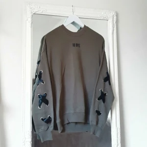 HI BYE militärgrön tröja H&M - Färg: milirätgrön/brun.  Strl: XS.   Snygg och skön tröja från H&M. Detaljer av broderad text på bröstet samt satinband som går från ärm till ärm via ryggen. Mjukt fodring inuti, inte nopprig eller annat slitage. Använd endast 1 gång, nyskick!!