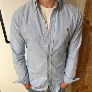 Ljusblå skjorta från Ralph Lauren - En stilren ljusblå skjorta från Ralph Lauren. Skjortan är fel fri och sitter något stort på modellen som är 174 cm.