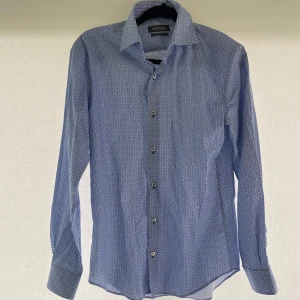 Långärmad skjorta - Stilig långärmad skjorta i ljusblå färg. Köpt hos Dressman. Ej använd. Perfekt till sommaren och finare tillställningar. Storlek: S (slim fit). Hör av er vid eventuella frågor!!