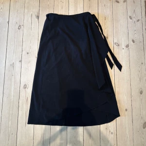 Svart omlottkjol - Svart omlottkjol, perfekt till sommaren. Knytning i sidan. I använt men bra skick. 