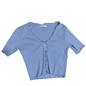 Ljusblå Pigalle tröja  - En ljusblå tröja med knappar, relativt stor för sin storlek som är XS men skulle säga att den lutar mer mot storlek S.