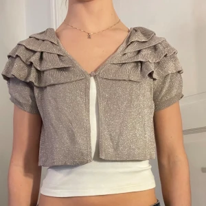 Glittrig bolero - Glittrig silvrig bolero med volanger. Storlek m men passar också s, xs. 