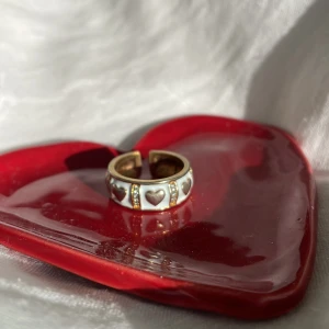 Guldring med hjärtan - Guldring med hjärtan och stenar (alla stenar är kvar). Går att justera där bak. Köptes i en liten butik utomlands, vågar inte svara om det är äkta silver eller ej, men det är vad butikspersonalen sa vid köp. Ca 18mm i diameter dvs storlek 8/57.