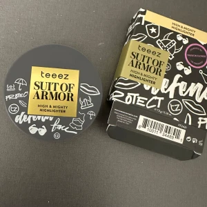 Suit of Armor High & Mighty Highlighter - En högkvalitativ highlighter från Teeez i nyansen 'Golden Girl' (MO120). Denna highlighter ger en strålande guldglans och är idealisk för medium till olivfärgade hudtoner. Produkten har en ultrafin puderformel med pärlpartiklar som ger en genomskinlig täckning och en omedelbar lysande finish. Förpackningen är grå med en spegel inuti. helt oanvänd
