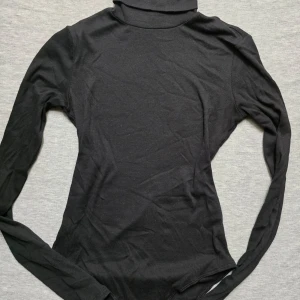 Elegant Svart Turtle Neck-Body - Säljer en elegant svart turtle neck-body i storlek XS. Denna figurnära och bekväma body är perfekt för både vardag och fest. Håller formen fint och är ett stilrent tillskott till garderoben. Passar utmärkt att bära under kavajer, tröjor eller för sig