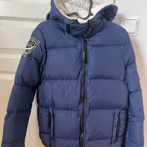 D brand dunjacka  - Jätte varm dunjacka, har aldrig frusit i den. Lite sminkrester på kragen och i luvan som ej går bort i tvätten. Det gröna på kardborren är från en tennisboll från tvätten. Annars inga defekter 