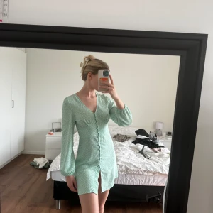 Klänning med knappar - Jättefin klänning med knappar från Nelly X Glamorous. Ganska kort i modellen. Endast använd 1 gång. Har tyvärr ett fäste till en knapp som gått upp (se sista bilden) går säkert lätt att fixa! Köpt för fullpris 449:-