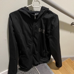 Emporio Armani Regnjacka  - Säljer nu en EA7 regnjacka som är i bra skick, finns några extremt små hål på ena armen,  men bortsett från det så är den i bra skick.  Priset är inte hugget i sten, så förhandling av priset är möjligt! Måste bort! ☺️