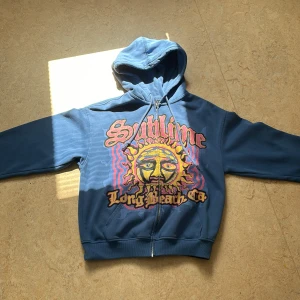 Blå hoodie med en sol på - Bra skick, dragkedja, skön att ha på sig, helt blå på baksidan 