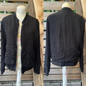 Så fin tunn jacka passar både till vardags och fest  - Så fin tunn jacka i viskos, vackert diskret mönster (svart i svart) skimrar diskret. Knappt anv i mycket fint skick! Passar både till vardags och fest. Både som jacka på sommarn och blus på hösten. Normal i storlek, två fickor framtill. 