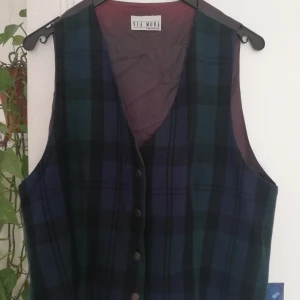 Väst blå grön svært rutig. Storlek S - Storlek S. Knappar framtill. Mörkrött foder. Små märken vid knappar och lite noppor-se bilder. 