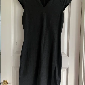 Svart klänning - En elegant mörkgrå klänning med korta ärmar och v-ringad hals. Klänningen har en enkel och stilren design som passar för olika tillfällen. Figursydd 