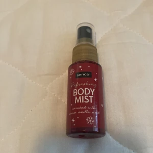 Refreshing Body Mist - En uppfriskande body mist från Sence, berikad med en varm vaniljdoft. Flaskan är röd med vita snöflingor och text.