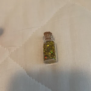 Glittrande ögonskugga i glasflaska - En liten glasflaska med kork innehållande glittrande ögonskugga i guld. Perfekt för att lägga till en gnistrande effekt på ögonlocken.