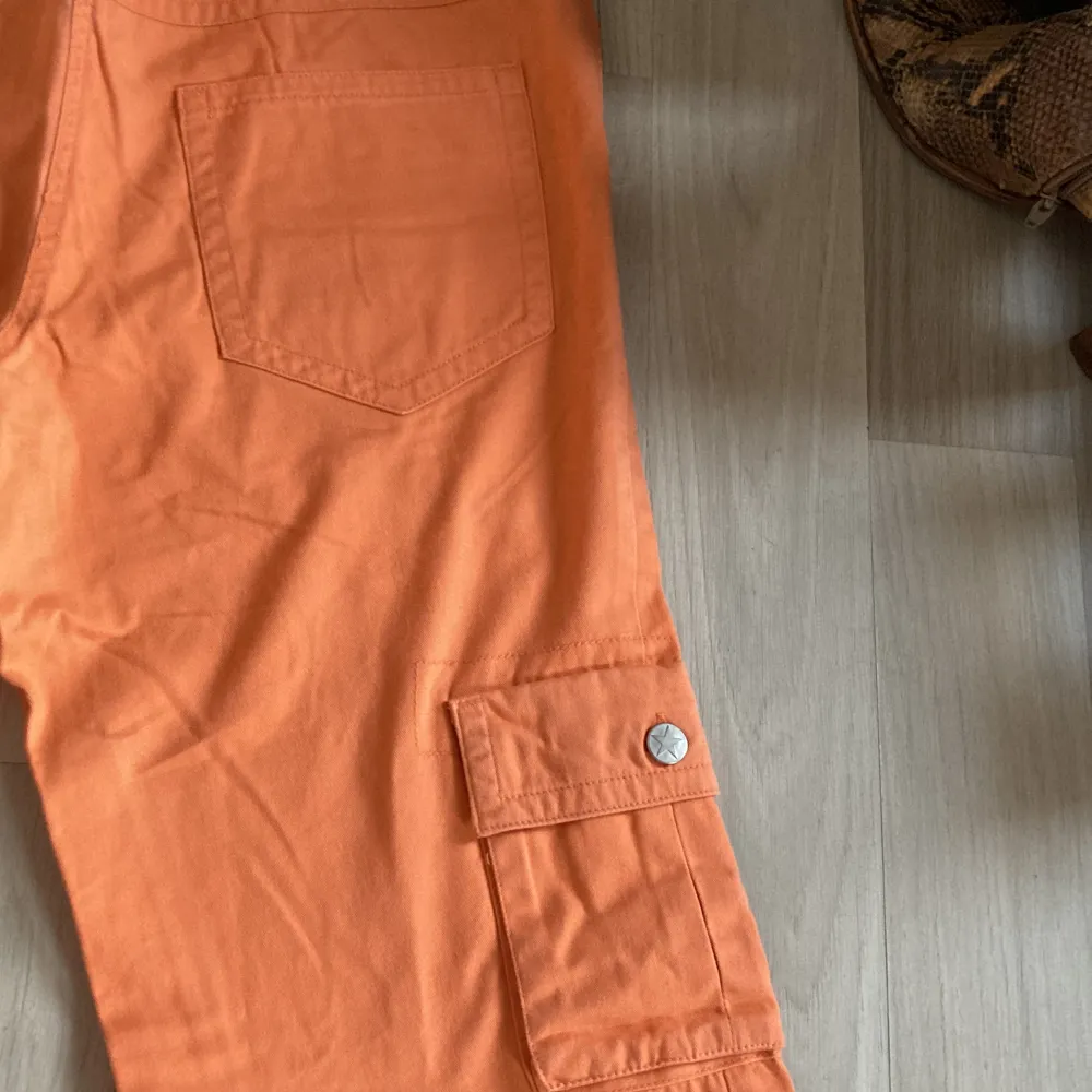 Jättefina lågmidjade orange byxor med blommor på sidan av benen och en ficka. Verkligen jättefina detaljer!🧡. Jeans & Byxor.