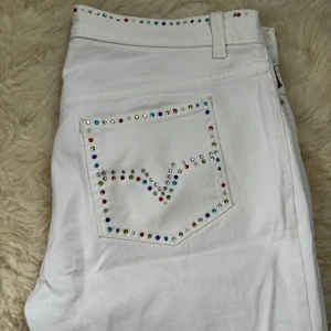 Vita Versace jeans  - VINTAGE Jeans från Versace. Detaljer med färglada stenar runt midja och på ena bakfickan. Använda men gott skick.