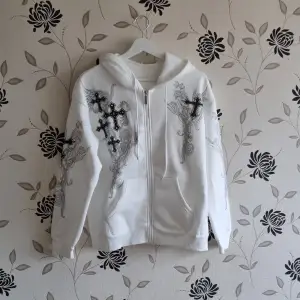 Vit hoodie med zip i Y2K-stil, den har tryck med kors och en dragkedja med fickor i fram. Nyskick!