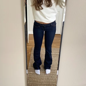 Lågmidjade jeans - Ett par mörkblåa jeans med orangea sömmar! Dom är lågmidjade och utsvängda. Långa i benen på mig som är 168cm.  Innerbenslängd: 87cm Midja: 80cm