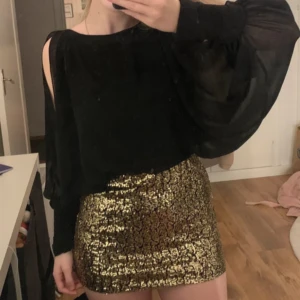 Kort klänning  - Aldrig använd. Öppna armar och knappar längst ner på armarna. Storlek 6/ XS. Guldiga paljetter. 