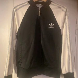 Adidasjacka  - Jättefin Adidasjacka med snyggt innerfoder och glitterstreck på ärmarna, köpt i usa så storleken är lite mindre än en svensk 44:a