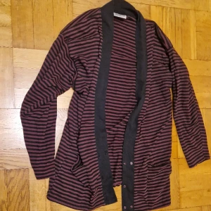 Randig cardigan - Lila/svartrandig cardigan med fickor och lila knappar nedtill. Stor och skön. Okej att komma med egna bud. Katt i hemmet. 