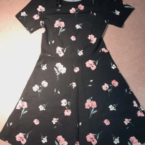 Svart klänning med blommor  - En kortärmad svart klänning med blommor. Väldigt söt modell där kjolen går ut lite. Från h&m divided i storlek 36. Använd några gånger, mycket fint skick. 