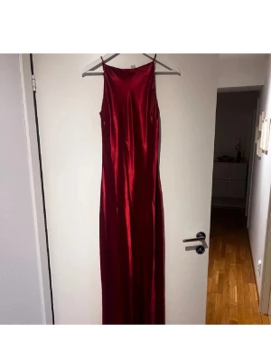 Vinröd satinklänning - Säljer en elegant röd långklänning med tunna axelband och rak passform. Storlek S och aldrig använd 