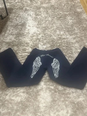 Mörkblå leggings med vingar som kostade 400kr - Säljer ett par mörkblå leggings med coolt tryck av vita änglavingar och texten 'Ma chérie' på baksidan. Byxorna har en slim passform och är gjorda i mjukt stretchigt material som sitter skönt. Perfekt för dig som vill sticka ut med en unik detalj.
