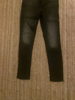 Svarta Skinny Liam jeans - Svarta jeans från Skinny Liam med skinny fit och klassisk femficksdesign. Jeansen har en mörk tvätt och smal passform som sitter tajt längs benen. Materialet är jeans och de har en stilren look med svarta detaljer och diskret etikett bak i midjan.