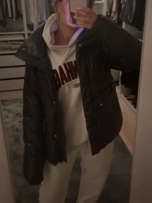 Indiska pufferjacka - Säljer en svart pufferjacka från indiska  med hög krage och stora fickor framtill. Jackan är quiltad och har dragkedja samt knappar. 