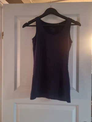 Mörkblå linnetopp från Lindex - Säljer en enkel och stilren mörkblå linnetopp från Lindex i ekologisk bomull. Toppen är ärmlös med rundad halsringning och har en rak passform som funkar till många olika looks. Perfekt för varma dagar eller som lager under en skjorta.