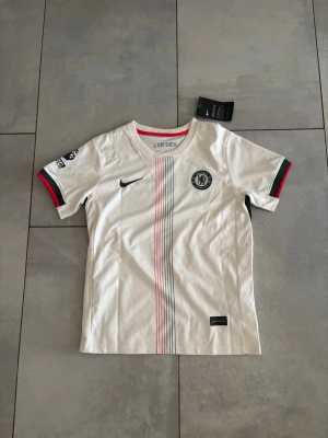 Chelsea FC fotbollströja med shorts - Chelsea FC tröja med Cole Palmer på ryggen. Shorts medföljer. Helt ny med lappen kvar, säljer för den va för liten för min lillebrorsa. Storlek 26 motsvarar ca 152/160 barnstorlek.