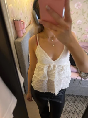 Vit volang linnetopp från Gina Tricot - Säljer en vit linnetopp från Gina Tricot i storlek S. Toppen har smala axelband, v-ringad hals och dubbla volanger framtill. Materialet är lätt och krusat, vilket ger en cool textur. Perfekt för varma dagar och snygg att styla med jeans eller kjol.