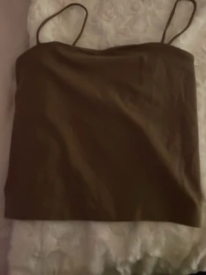Brun linnetopp  - Säljer en enkel brun linnetopp med smala axelband och rak skärning. Toppen är ärmlös och har en stilren, minimalistisk look som passar perfekt till varma dagar. Materialet känns mjukt och lätt mot huden. Från Gina tricot
