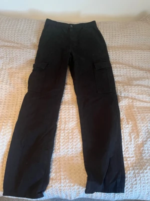 Svarta cargopants med raka ben - Svarta cargopants med raka ben och stora fickor på sidorna. Byxorna har klassisk midja och bälteshällor - perfekt för dig som gillar streetwear och vill ha plats i fickorna. Aldrig använda.
