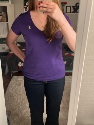 Lila t-shirt från Ralph Lauren  - Snygg lila t-shirt från Ralph Lauren Sport med v-ringning och korta ärmar. T-shirten har en grön broderad logga på bröstet och är gjord i mjuk 100% bomull. Perfekt för dig som gillar klassisk stil med en färgklick. Nypris ca 650kr! Därav priset